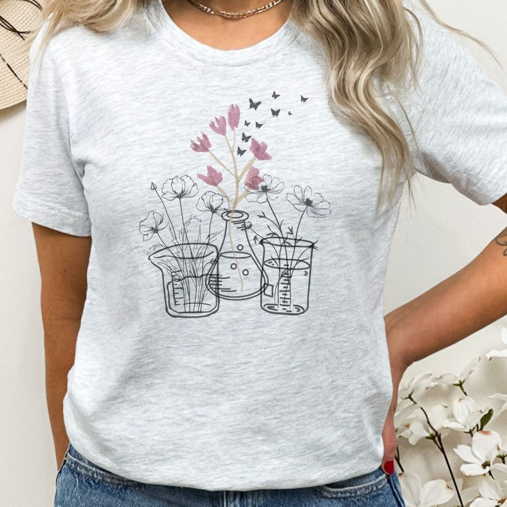 Ash-colored t-shirt featuring a floral science design with flowers growing from lab beakers and flasks, ideal for lab technicians who enjoy blending science and nature with a casual, comfortable look.