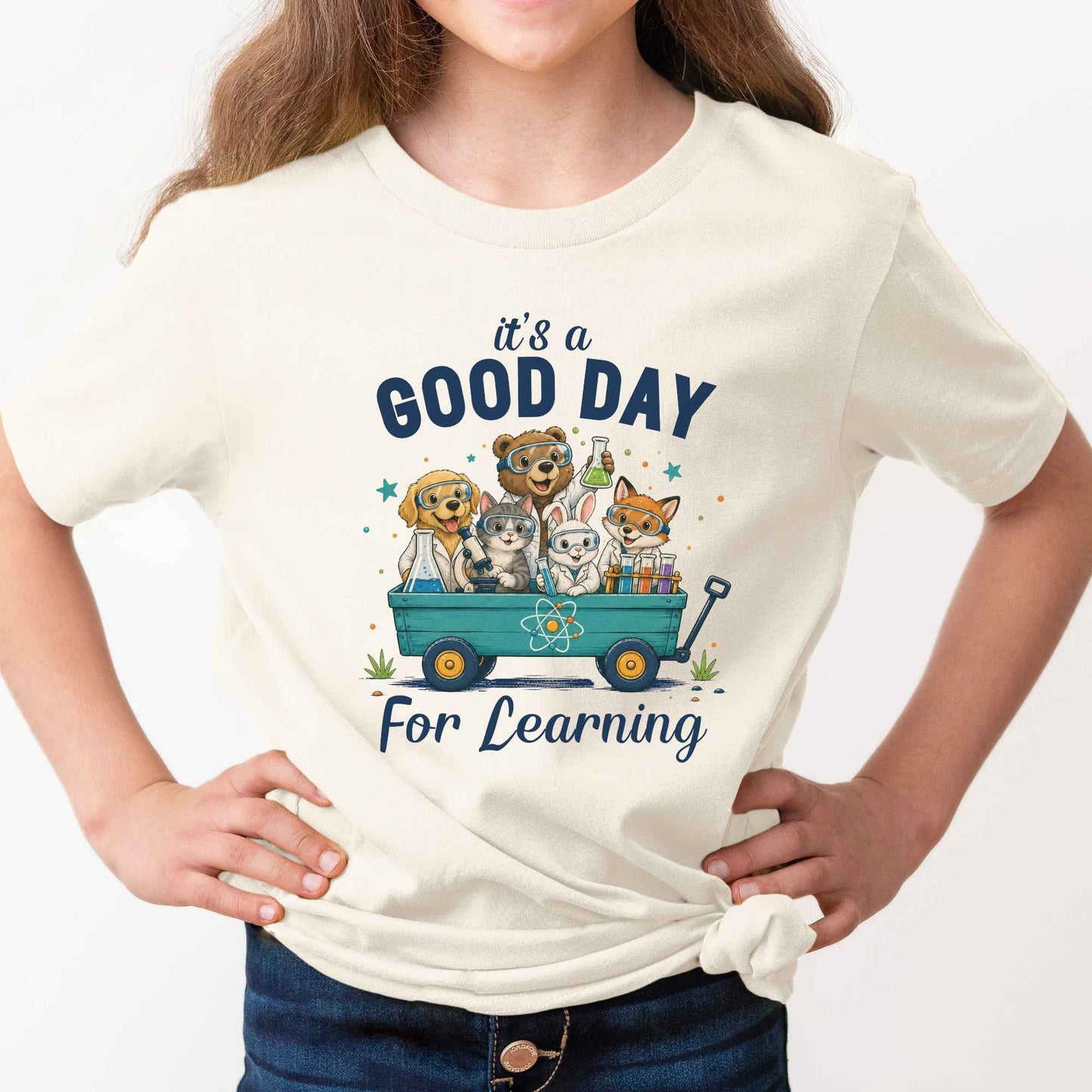 A child wearing a cream-colored graphic t-shirt with a cartoon illustration of dogs in a wagon and the text 'it's a GOOD DAY For Learning'.