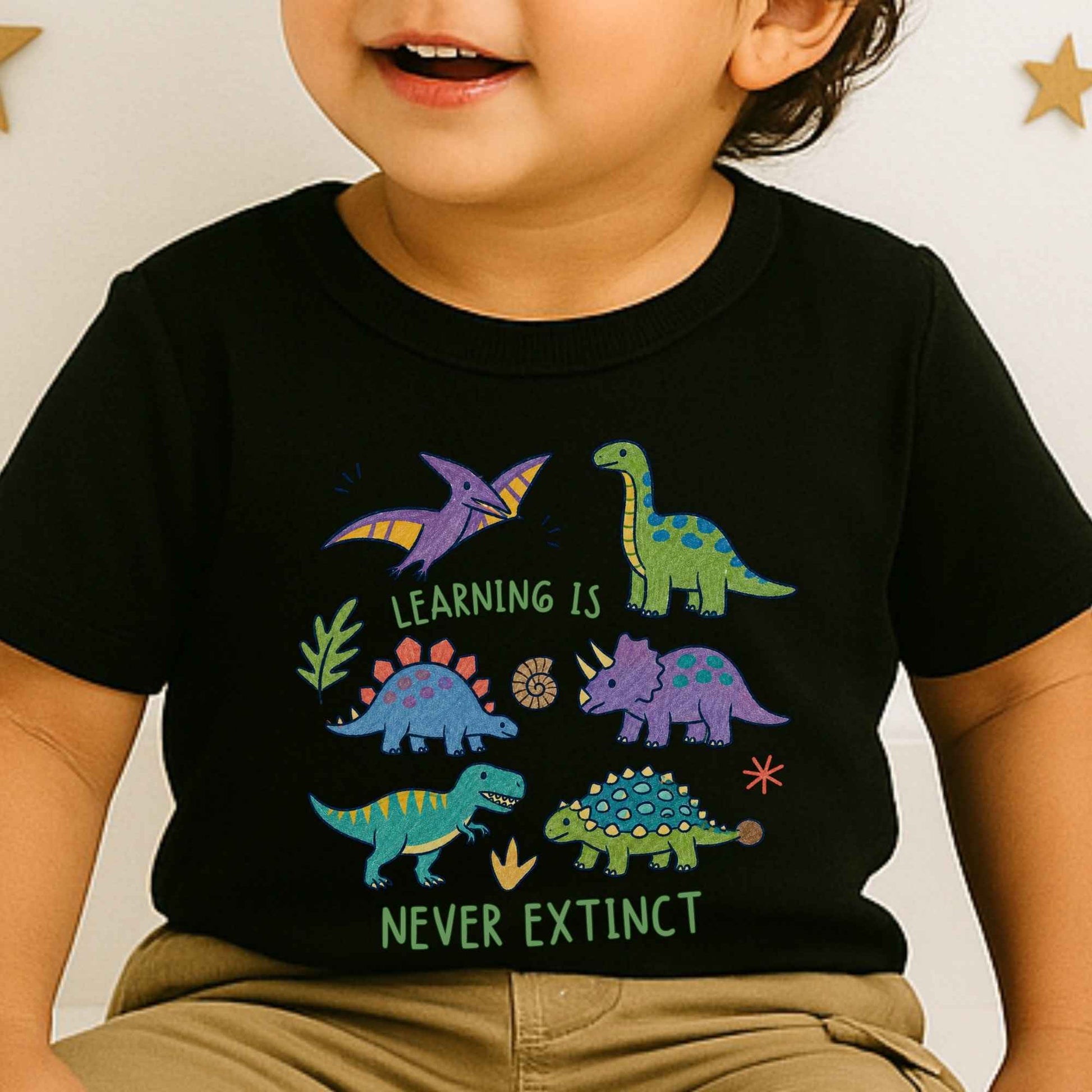 A close-up of a child wearing a black short-sleeve T-shirt with colorful dinosaur illustrations and the text 'LEARNING IS NEVER EXTINCT'.