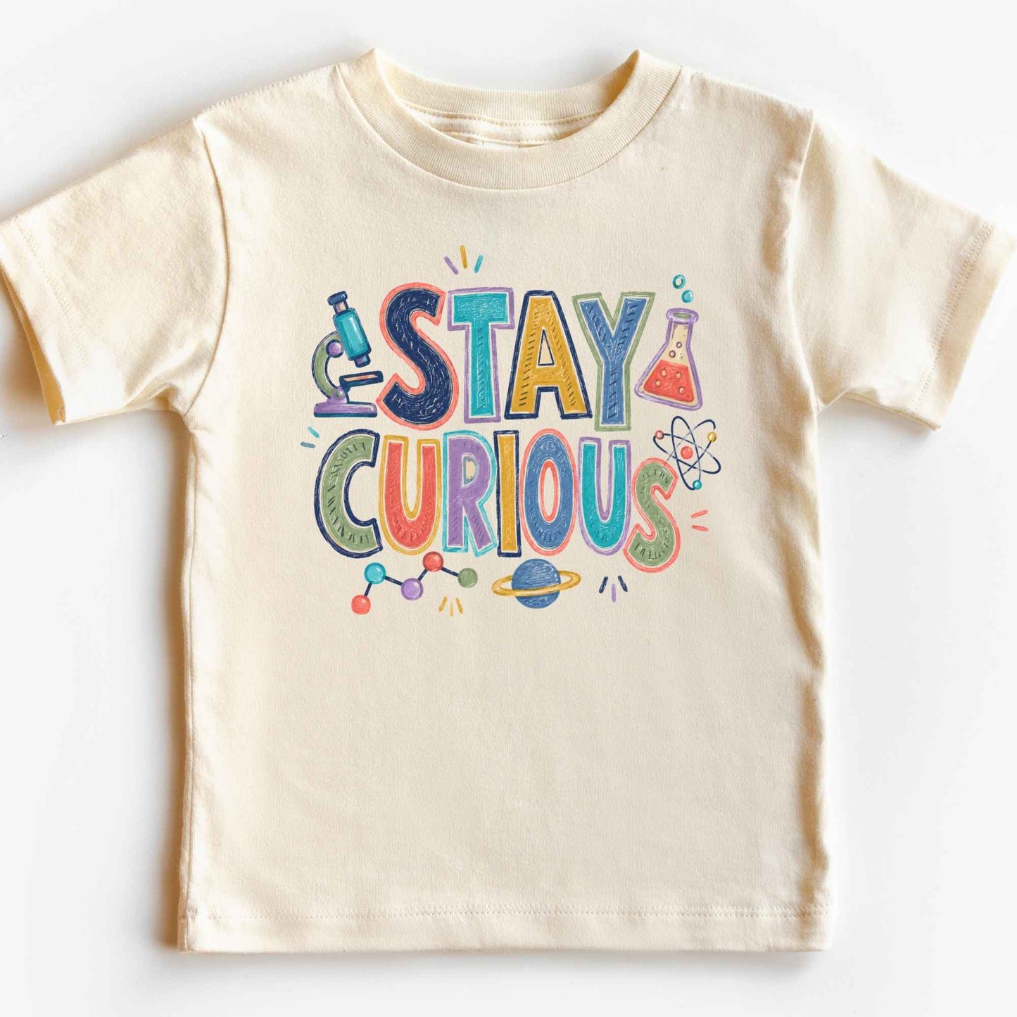 A cream-colored short-sleeve kids' t-shirt featuring a colorful 'STAY CURIOUS' graphic with science-themed illustrations like a microscope, beaker, and atom on a white background.