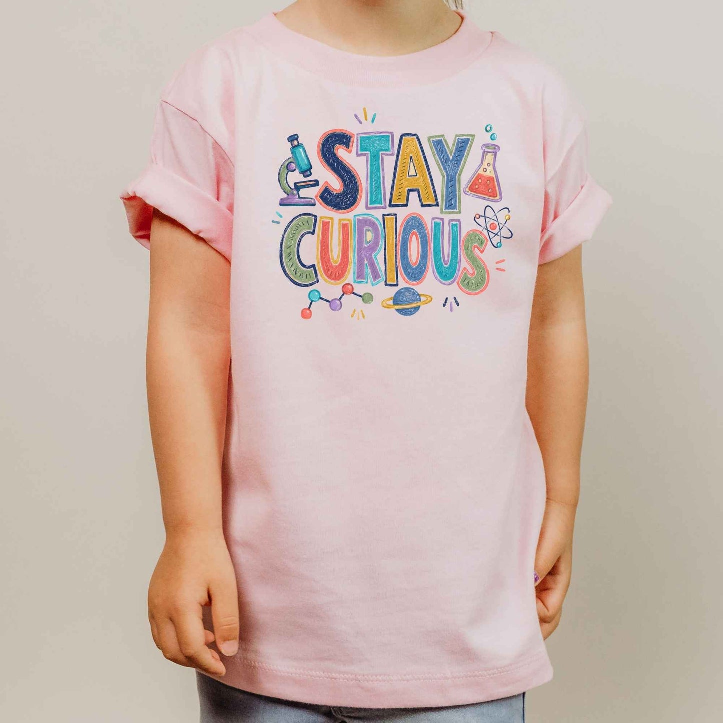 A child wearing a light pink short-sleeve t-shirt with a colorful 'STAY CURIOUS' graphic on the chest, set against a plain light gray background.