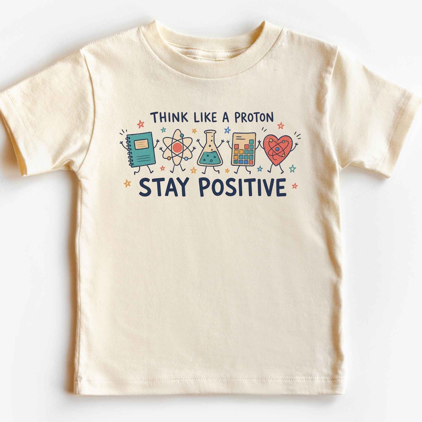 A cream-colored short-sleeve kids' t-shirt with a colorful graphic print that reads 'THINK LIKE A PROTON STAY POSITIVE' accompanied by cartoon illustrations of a notebook, atom, beaker, calculator, and heart.